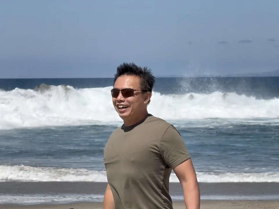 Dave smiling in sunglasses beside the sea.