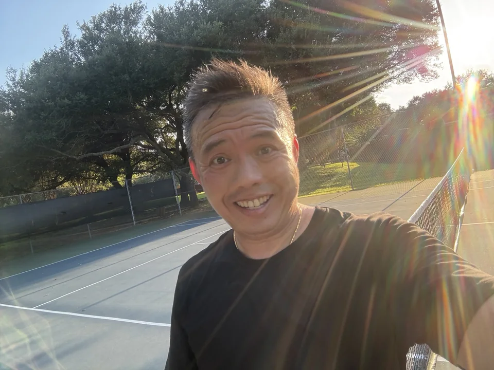 Dave smiling on an outdoor tennis court in the sunshine.