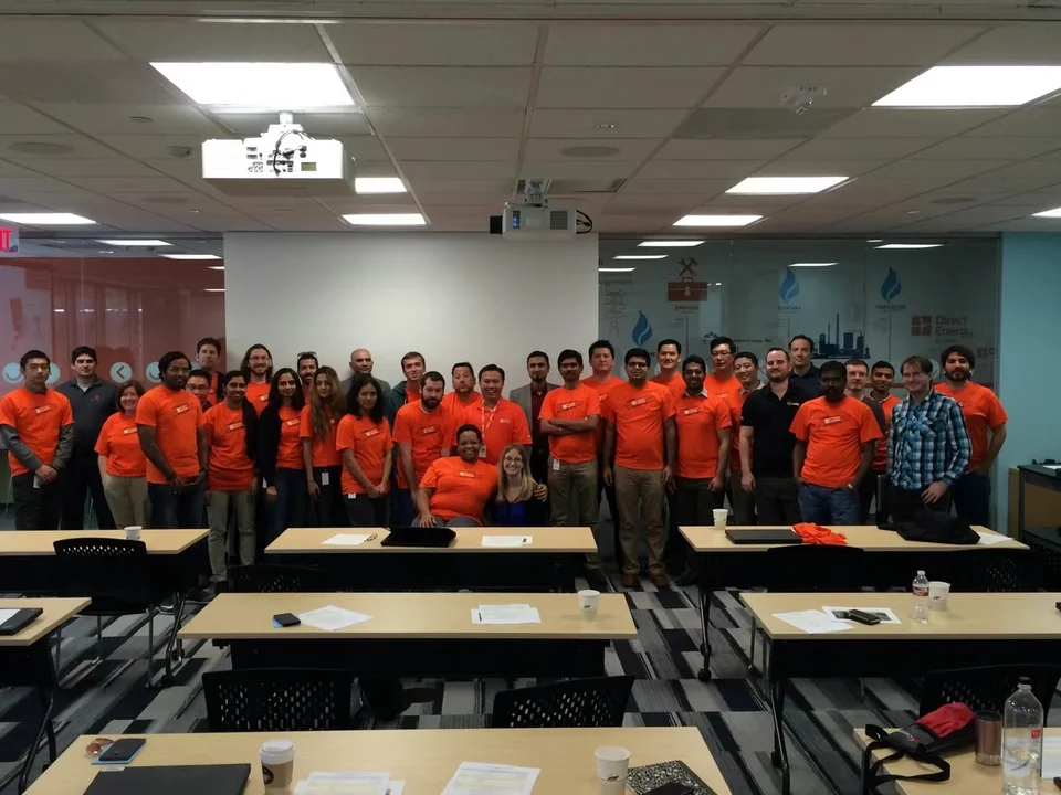 A group of colleagues, many wearing orange shirts, in a meeting room.